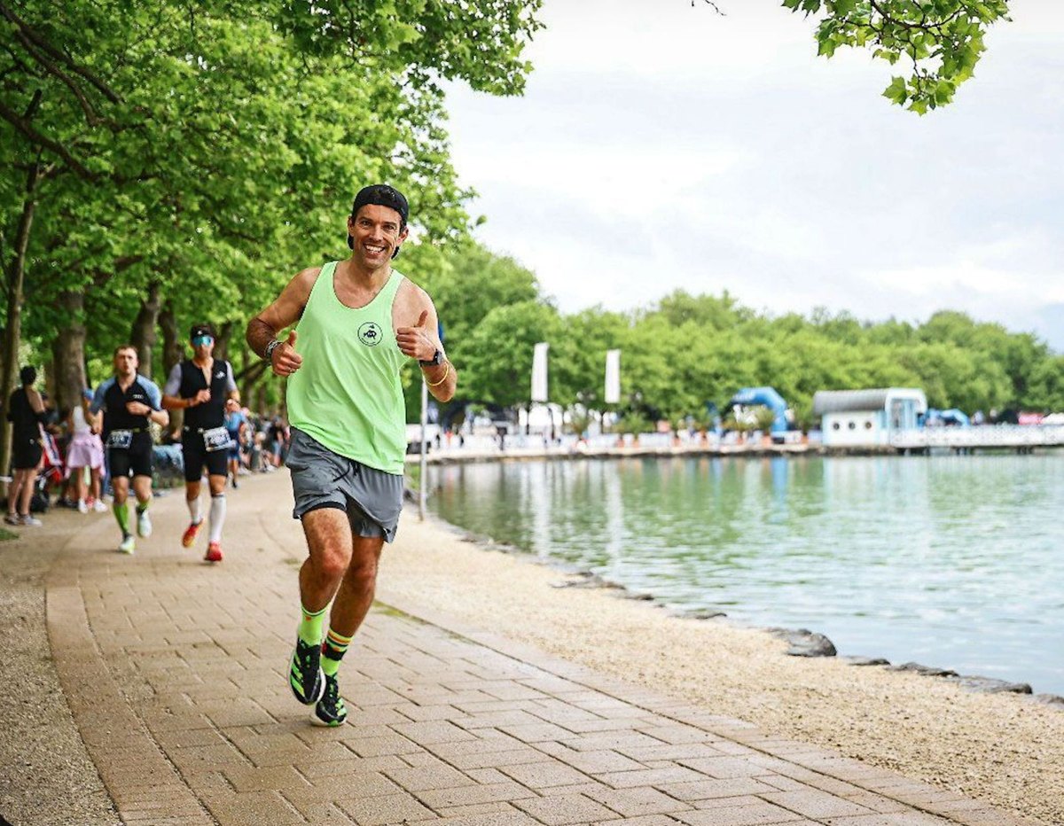 Corredor sonriendo y levantando los pulgares junto a un lago